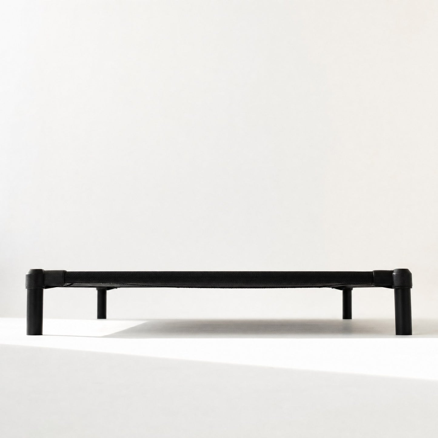 The cot seen at floor level, the gap underneath reading as a band