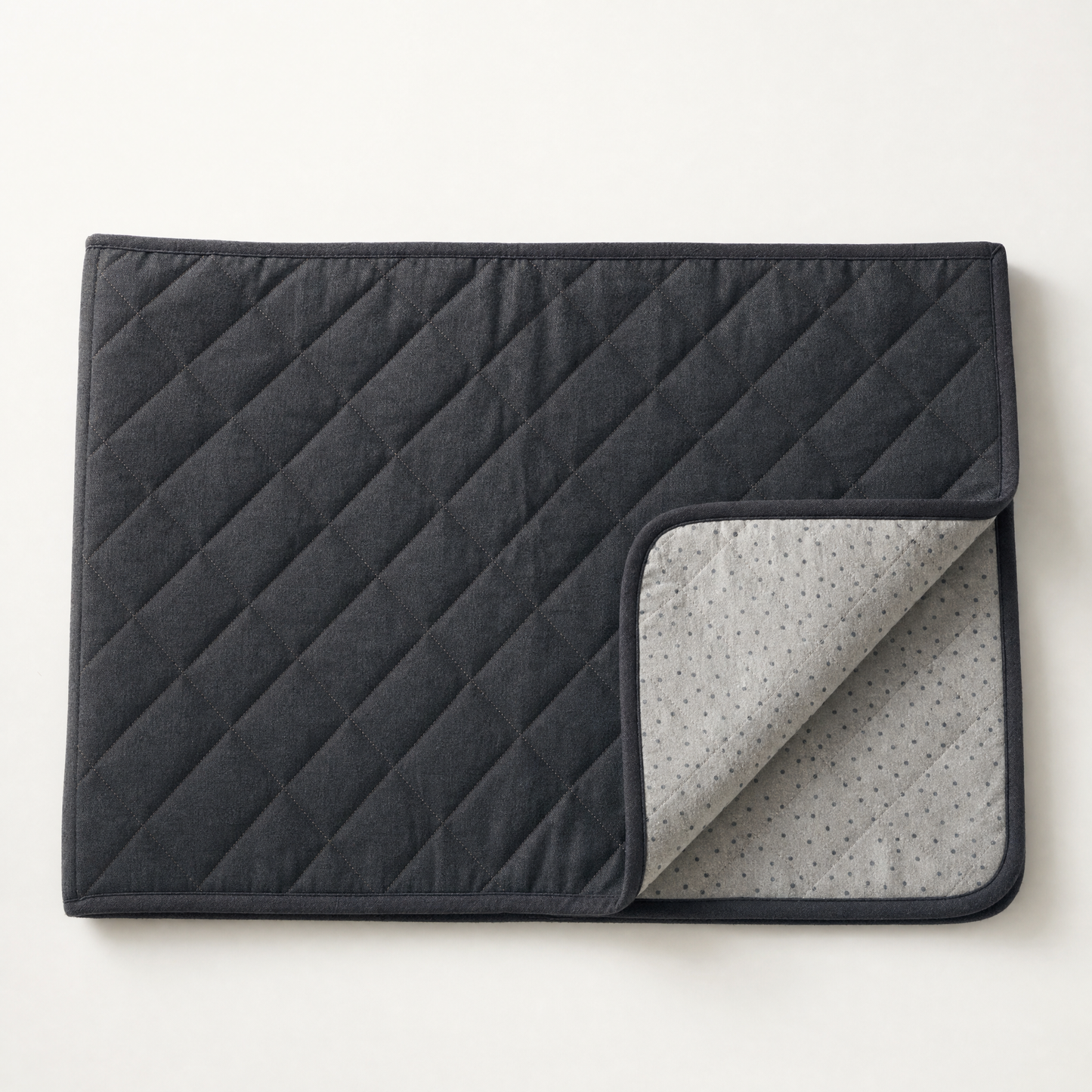 The charcoal quilted face and bound edge, one corner folded to show the grey backing